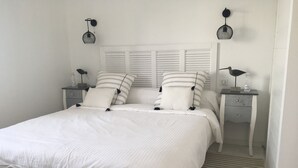 A neatly made bed with white bedding and striped pillows, two bedside tables with lamps, and a striped floor. - 180° sea view-Terrace-Rooftop-Plage-City center-Fiber-Netflix-Clim-Garage   (Arcachon)
