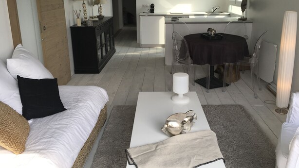 A modern living room with a white sofa, a coffee table with decorative items, and a view into the kitchen area.