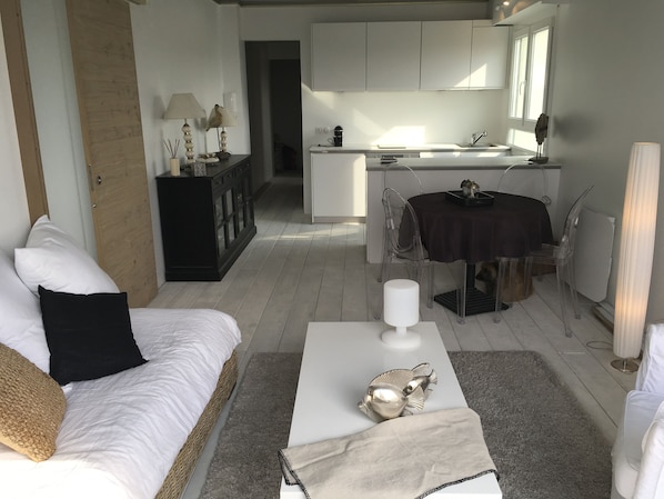 A modern living room with a white sofa, a coffee table with decorative items, and a view into the kitchen area. - 180° sea view-Terrace-Rooftop-Plage-City center-Fiber-Netflix-Clim-Garage   (Arcachon)