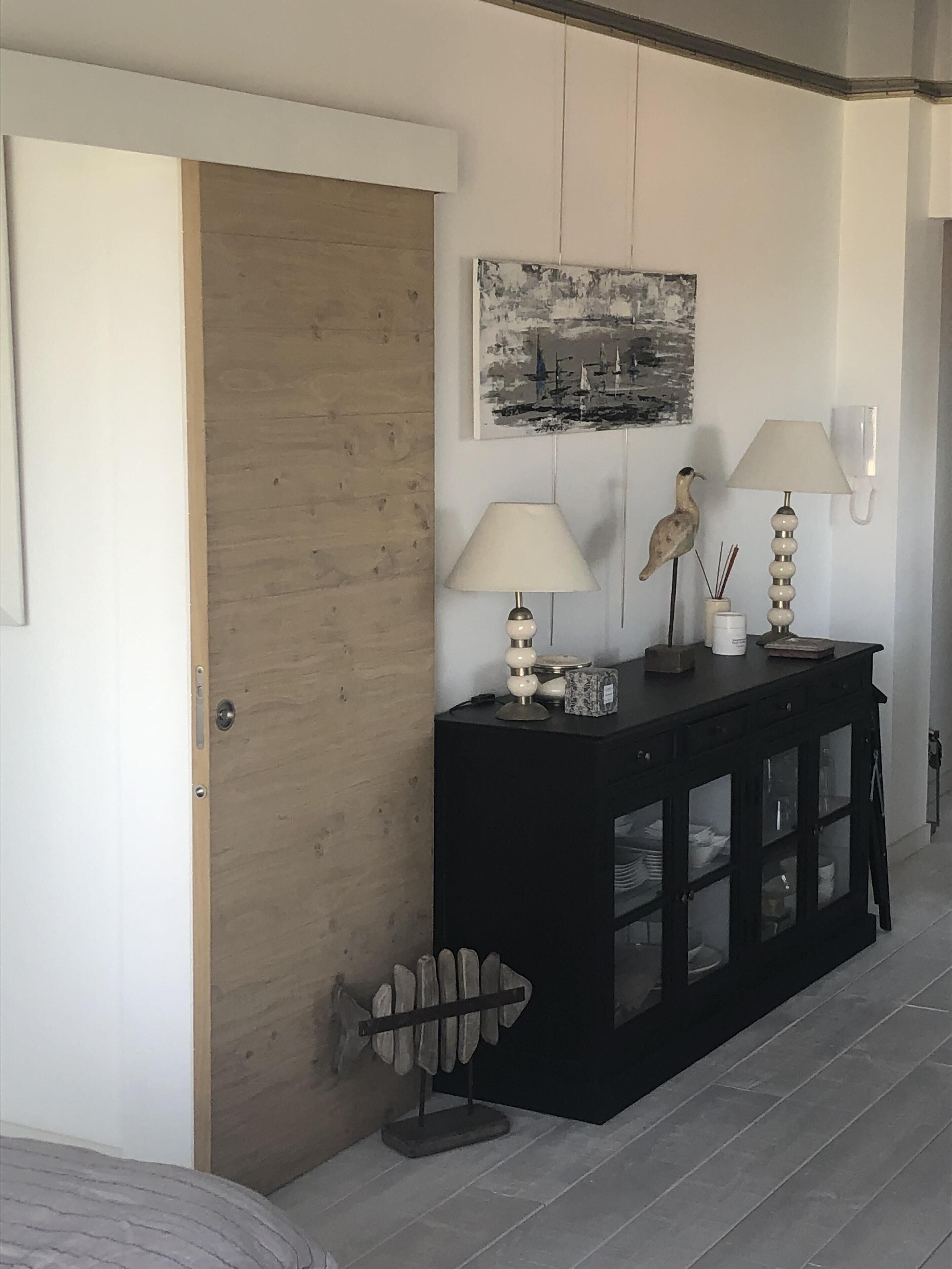 A room with a wooden door, a black console table with two lamps, a wall-mounted painting, and a decorative fish sculpture.