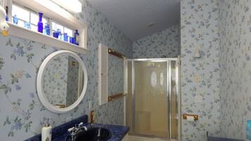 Een badkamer met een blauwe marmeren wastafel, een ronde spiegel, een douche met een glazen deur en bloemenbehang.