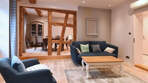 A modern living room with a dark blue sofa, a wooden coffee table, and a blue armchair. There is a dining area in the background with a wooden table and chairs. - Bredala ***, 5-person apartment in the historic center of Colmar - 2 bedrooms (Colmar)