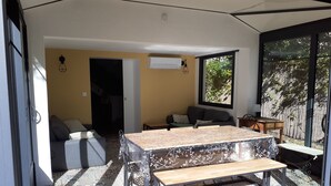 Une pièce baignée de lumière naturelle, avec un sol à motifs, un canapé, une table avec un banc, et une vue sur la verdure par une grande fenêtre.