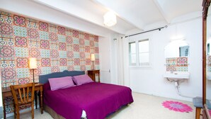 Une chambre à coucher comprenant un lit, un bureau, une chaise, un mur recouvert de carreaux décoratifs, une fenêtre et un miroir.