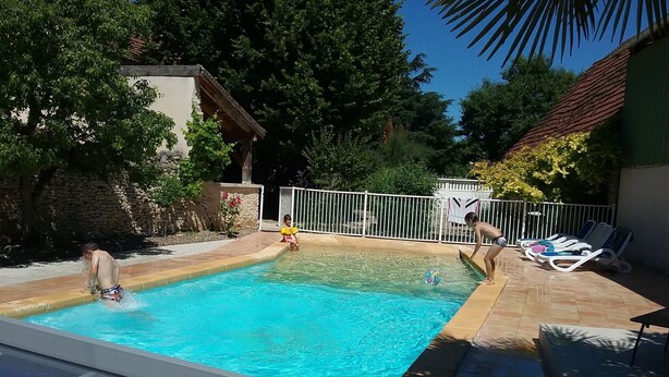Une piscine avec une terrasse carrelée, une clôture blanche et des chaises longues.