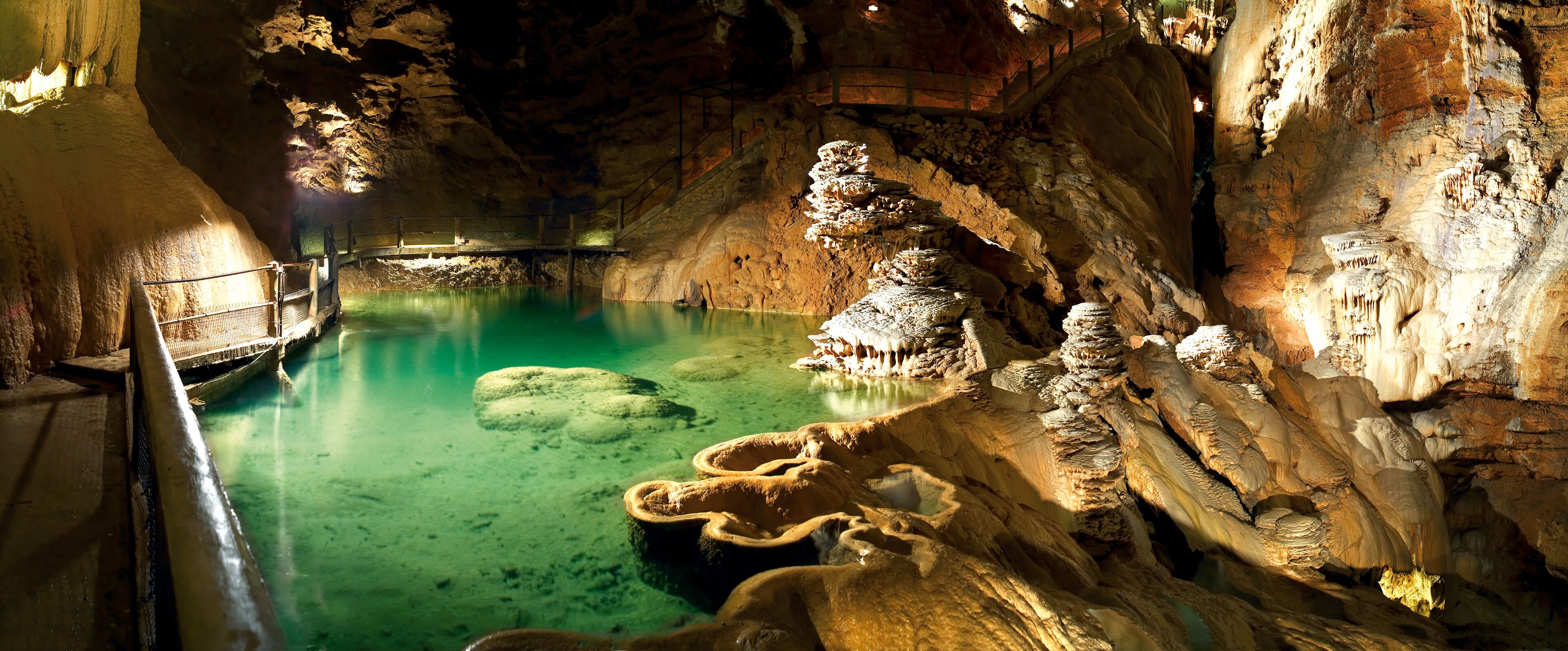 A cave with stalactites and stalagmites, a pool of water, and a wooden walkway.