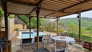 Uma área externa coberta com piscina, cadeiras de descanso e uma mesa.