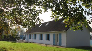 A white building with blue shutters and a tiled roof, surrounded by greenery.
