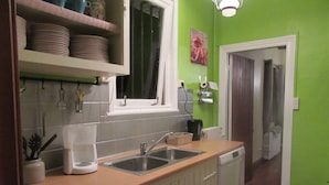 A kitchen with a sink, coffee maker, and a window. There are plates on a shelf above the sink and a picture on the wall.