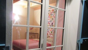 A room with a bed, a quilt, and a window with a view of another room.