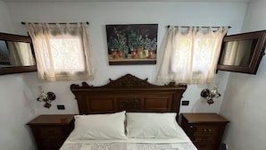 Cama bem arrumada com colcha estampada, duas mesas de cabeceira com abajures e um quadro sobre a cama.