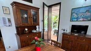 Uma sala de jantar com uma mesa e cadeiras de madeira, um vaso de flores vermelho e uma televisão em um armário de madeira.