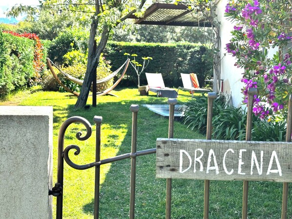Un jardín con una hamaca, sillones de descanso y un letrero de madera que dice 'DRACENA'.