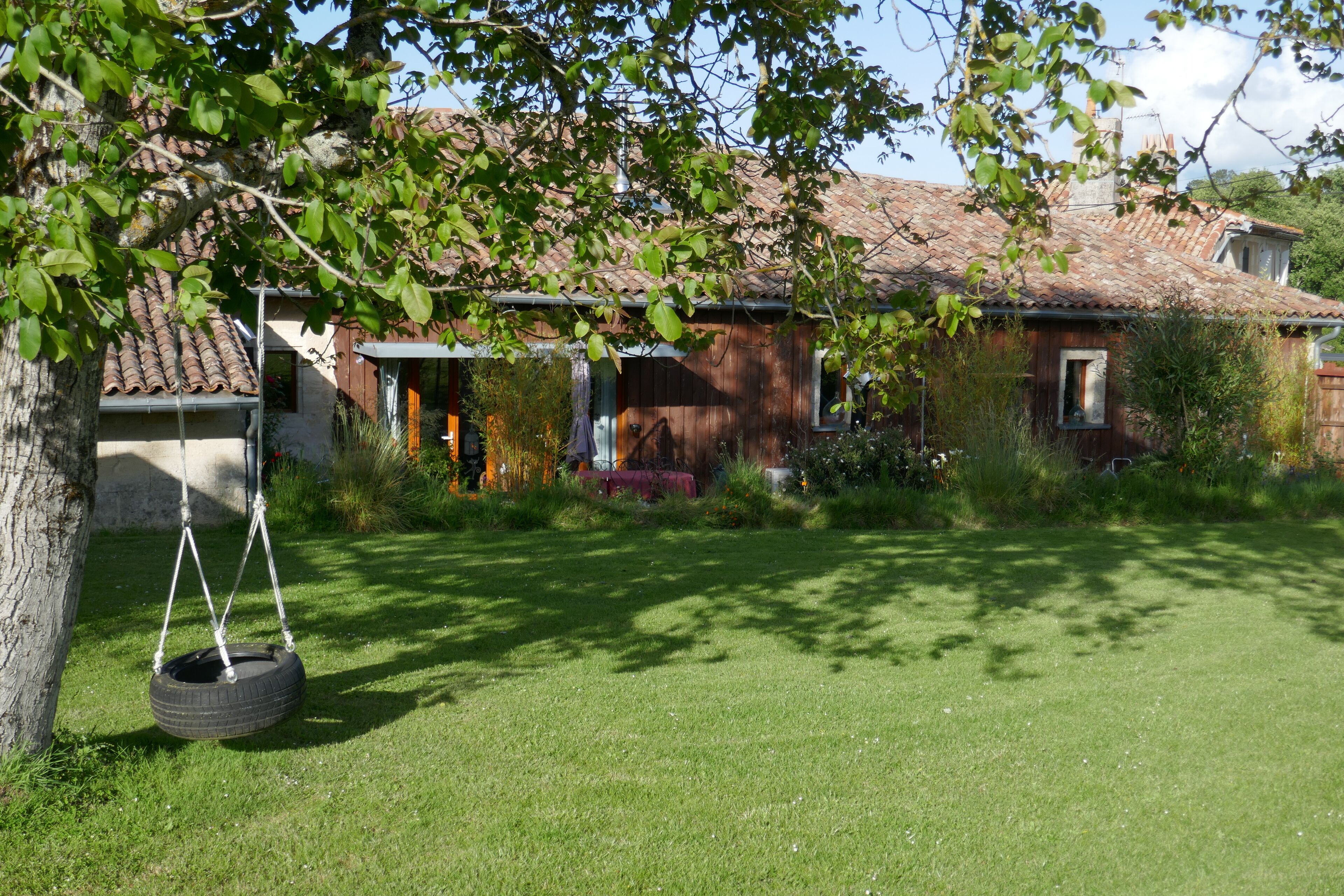 A rustic house with a tiled roof, a swing hanging from a tree, and a well-maintained lawn.