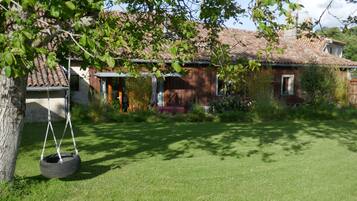 A rustic house with a tiled roof, a swing hanging from a tree, and a well-maintained lawn.