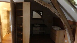 Une petite chambre mansardée avec un plafond en bois, une étagère intégrée et une petite salle de bain dotée d’un miroir et d’un lavabo.