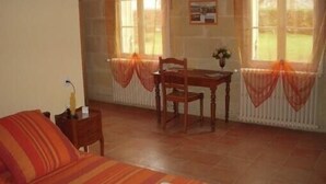 A room with a bed, a wooden table, and two chairs. There are curtains on the windows, and a picture is hung on the wall.