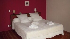A neatly made bed with white linens in a room with a red wall and a wooden headboard.