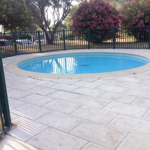 Uma piscina com revestimento de azulejos, rodeada por uma cerca verde e árvores com flores cor-de-rosa.