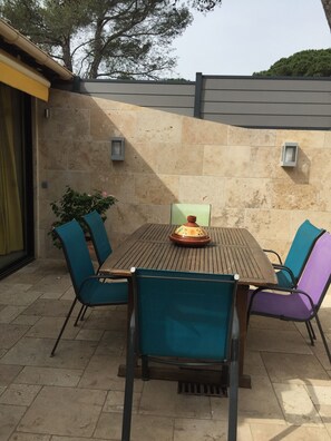 Um pátio externo com mesa de madeira e quatro cadeiras, cercado por paredes de pedra e vasos de plantas.