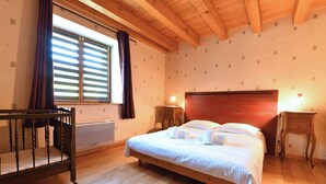 Un dormitorio con una cama de madera, una cuna, una ventana con persianas y dos lámparas de noche.