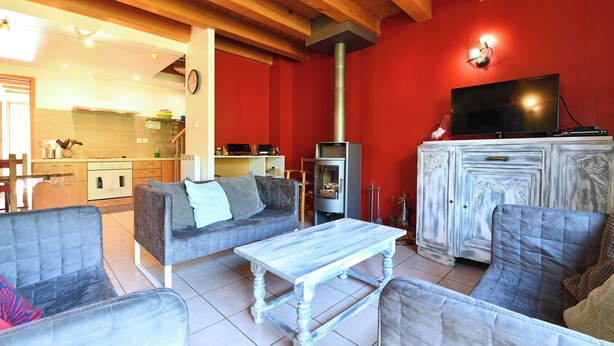 Una sala de estar con chimenea, televisor y comedor, con una cocina al fondo.