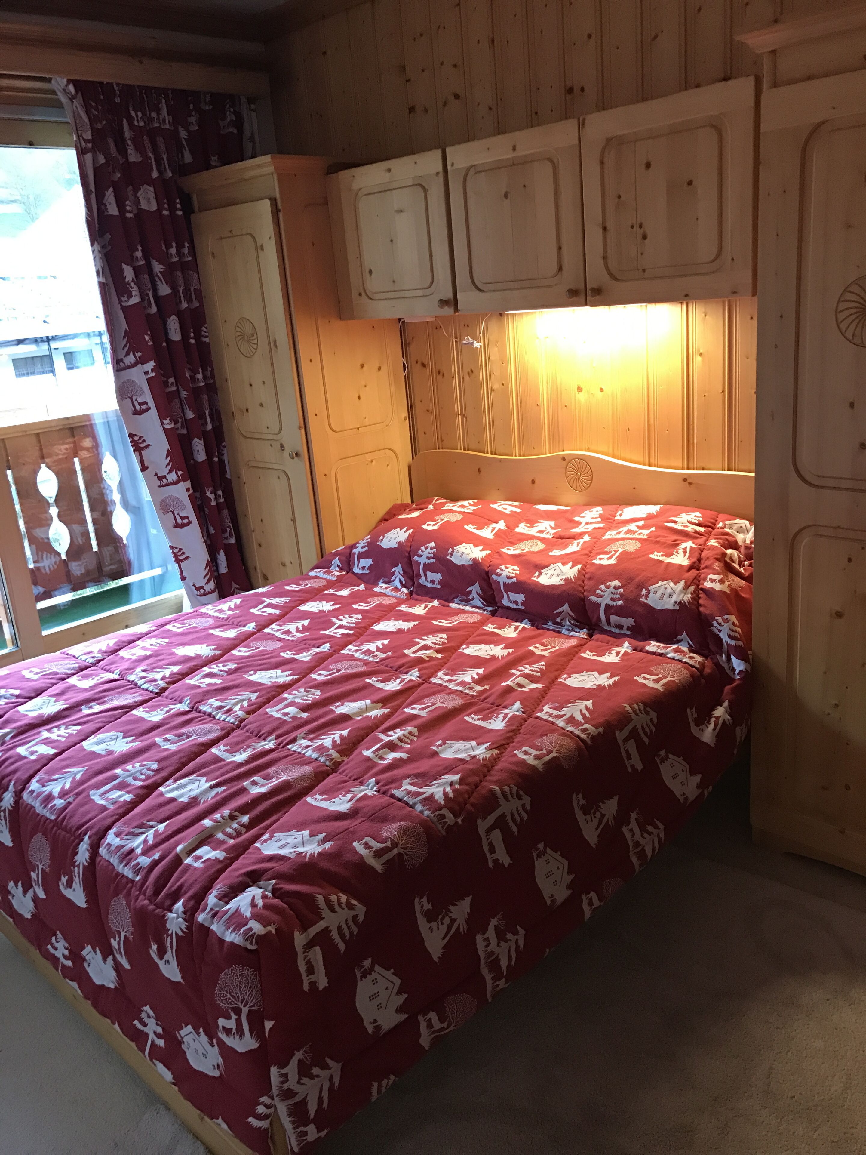 A wooden room with a bed, a window with curtains, and a wooden headboard.