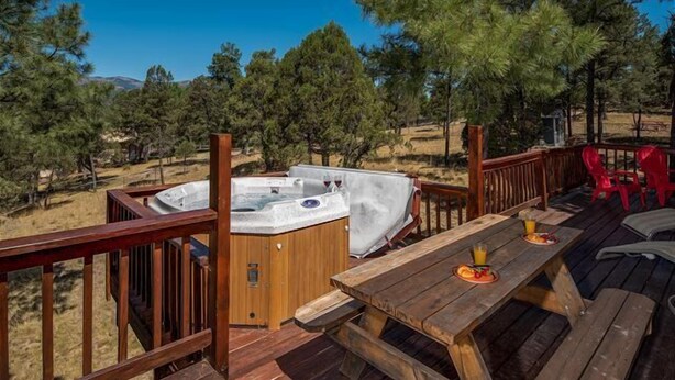 A wooden deck with a hot tub, picnic table, and red chairs.