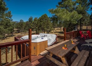 A wooden deck with a hot tub, picnic table, and red chairs. - Amazing Place, big, bold, beautiful with easy level access and paved parking (Ruidoso)