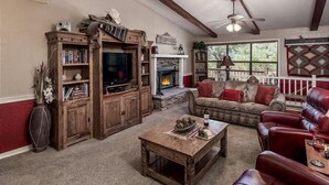 A cozy living room with a fireplace, leather sofas, a wooden entertainment center, and a ceiling fan.