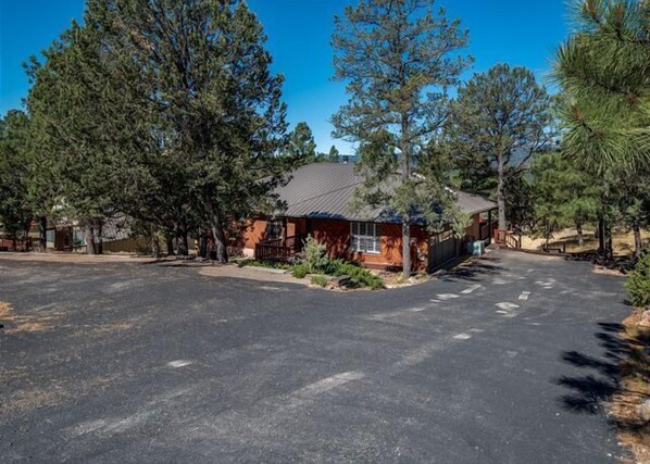 A single-story building with a sloped roof, surrounded by trees and a paved driveway. - Amazing Place, big, bold, beautiful with easy level access and paved parking (Ruidoso)