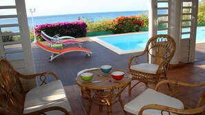 A poolside area with wicker furniture and a view of the ocean.