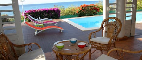 Área da piscina com mobiliário de vime e vista para o oceano.