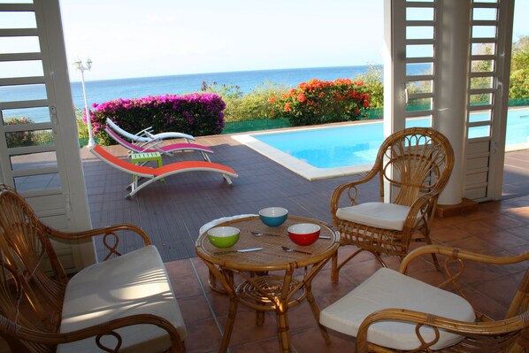 A poolside area with wicker furniture and a view of the ocean.