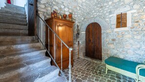 A stone-walled room with a wooden staircase, a bench, and a wooden cabinet.