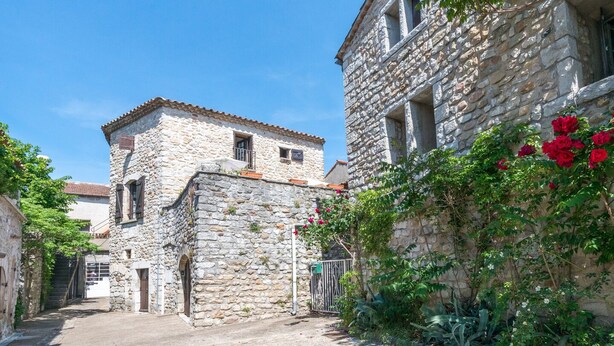 A narrow stone street with buildings on either side, one with a visible door and window, and another with a balcony.