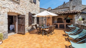 A stone building with a patio area featuring a table and chairs, a grill, and a potted plant.