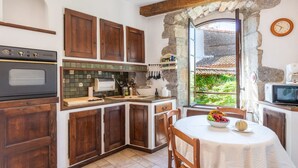 A compact kitchen with wooden cabinets, a built-in oven, a microwave, and a dining area with a table set for two.
