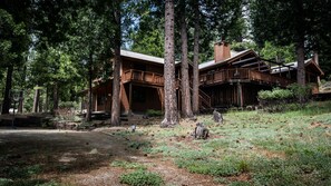 A rustic cabin with a wooden deck, surrounded by tall trees and a natural landscape. - Red Fox Property Graeagle/Blairsden (Clio)