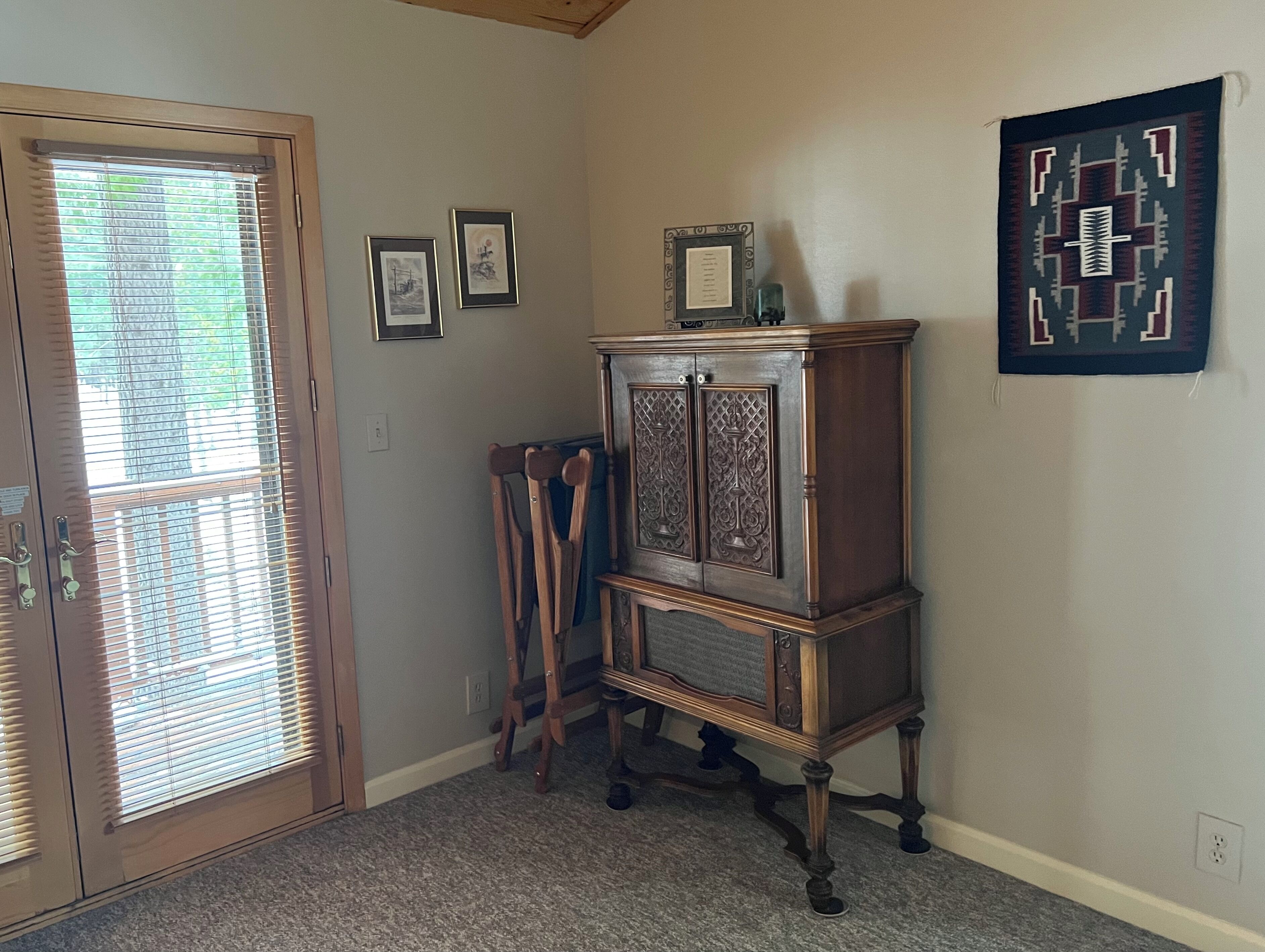 A room with a wooden cabinet, a door with blinds, and framed artwork on the wall.