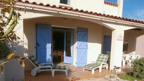 Un patio techado con dos sillones y una mesa, una puerta azul y un reloj en la pared.