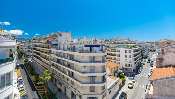 A multi-story building with balconies, a street with cars, and a clear blue sky. - Béatrice Apartment with free parking. Elevator (Nice)