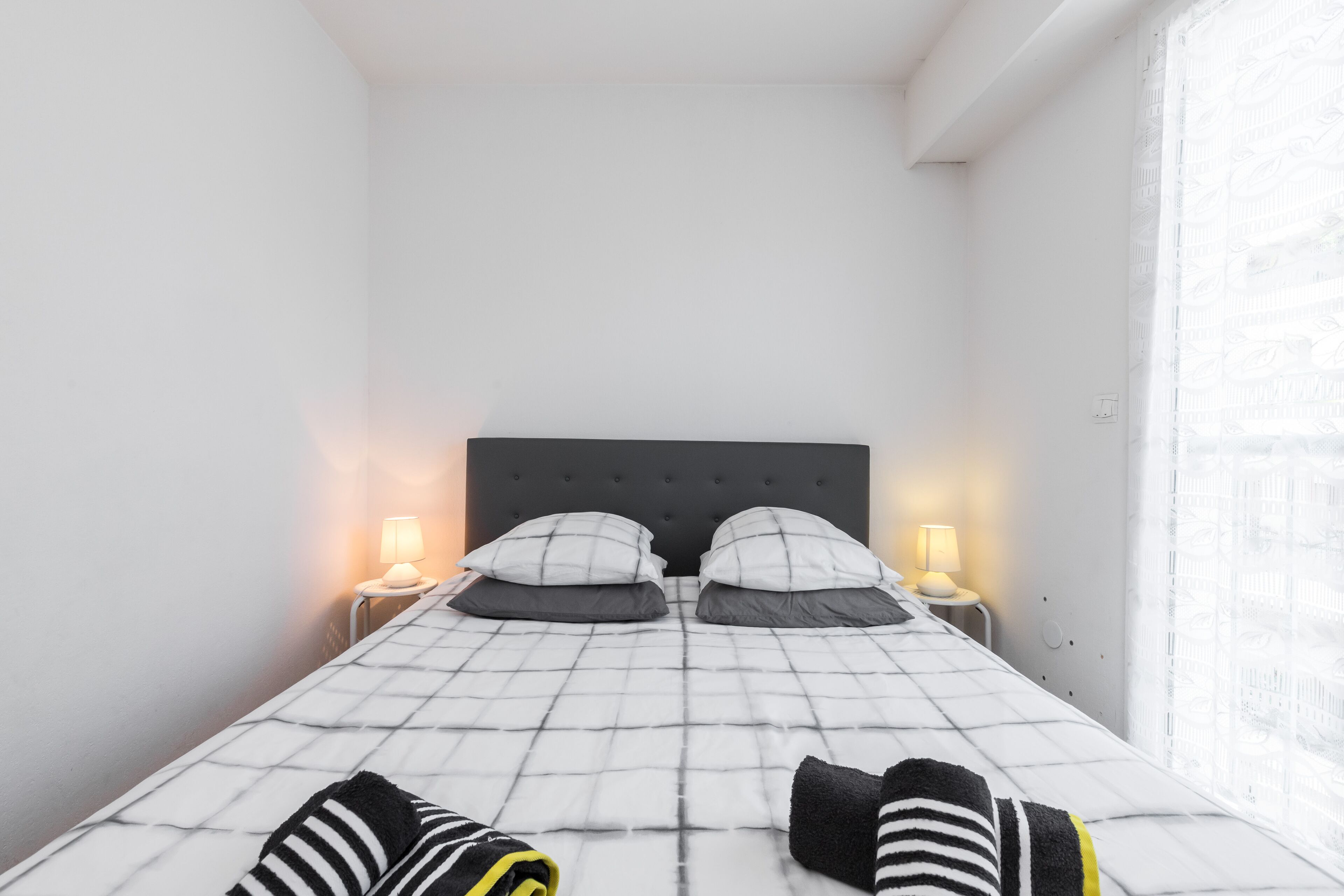 Un lit bien fait, recouvert d’une couvre-lit à carreaux noirs et blancs, avec deux oreillers et deux lampes de chevet.
