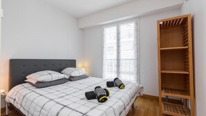 A bedroom with a bed, pillows, a wooden wardrobe, and a window. - Béatrice Apartment with free parking. Elevator (Nice)