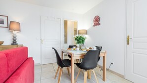 A dining area with a table set for two, black chairs, a red sofa, and a lamp on a side table. - Béatrice Apartment with free parking. Elevator (Nice)