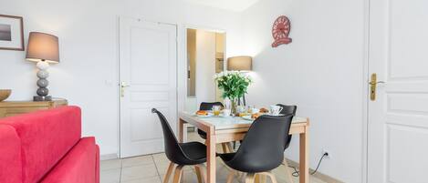 A dining area with a table set for two, black chairs, a red sofa, and a lamp on a side table.