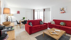 A modern living room with a red sofa, a wooden coffee table, and a dining area with a table and chairs. - Béatrice Apartment with free parking. Elevator (Nice)