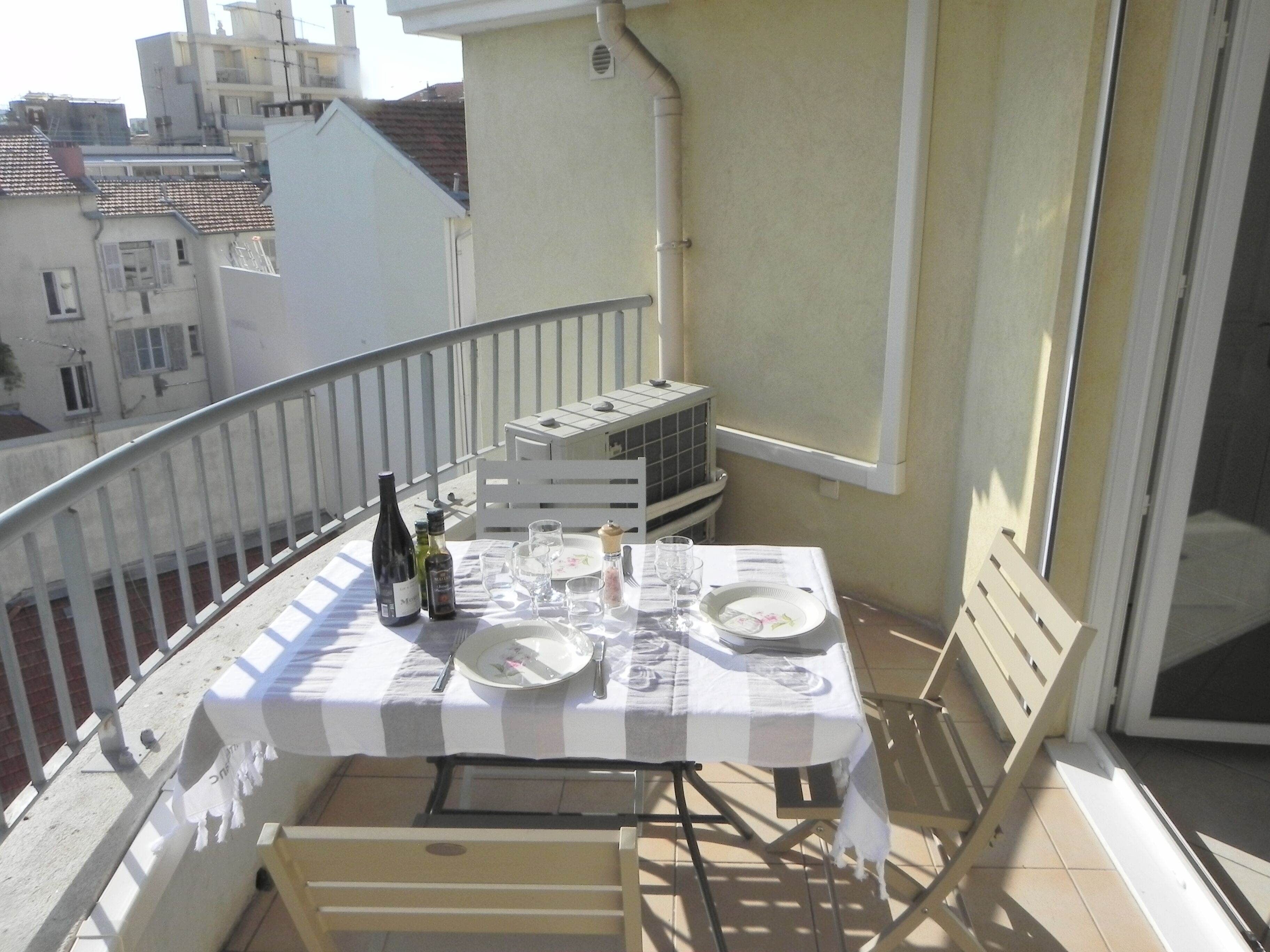A balcony with a table set for two, a bottle of wine, and a small table with a chair.