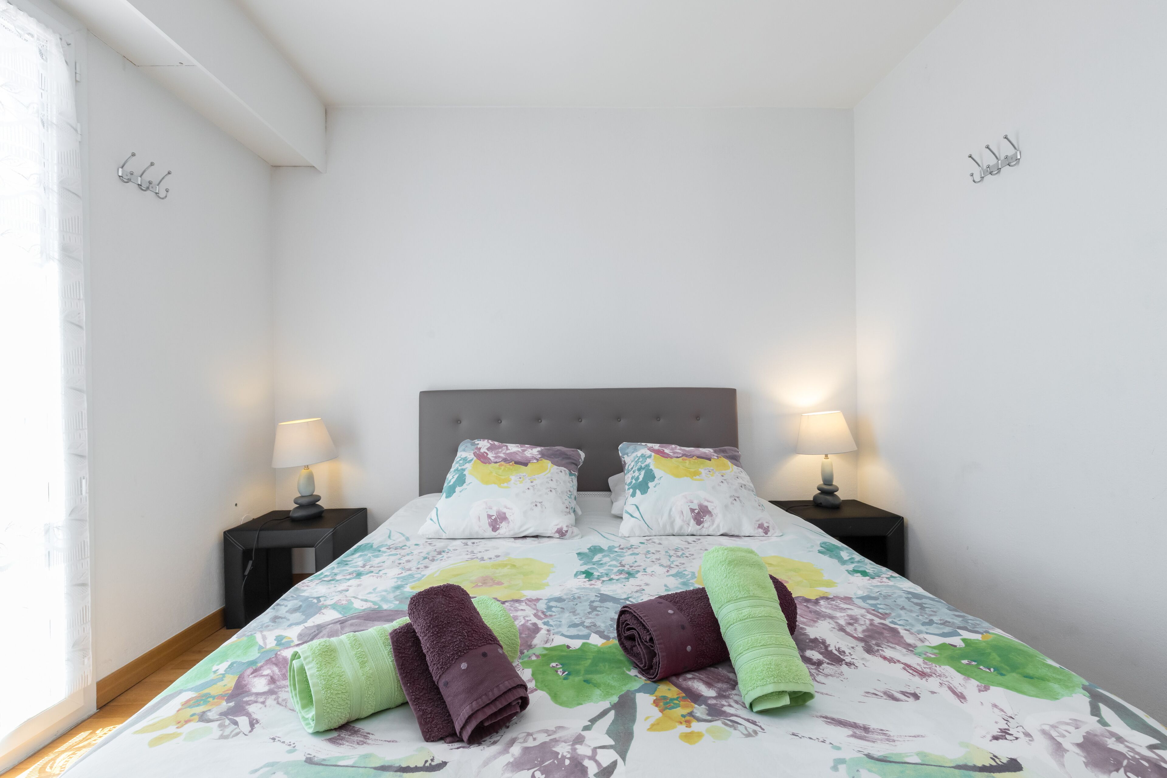 Un lit bien fait, avec une literie à motifs floraux, deux lampes de chevet et des serviettes enroulées posées sur le lit.