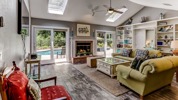 A spacious living room with a fireplace, a pool view, and a ceiling fan.